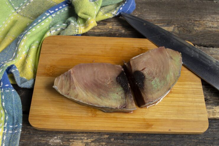 Preparing Tuna Steak - Patting the thawed tuna dry with a paper towel. A raw tuna steak being patted dry with a white paper towel on a cutting board.