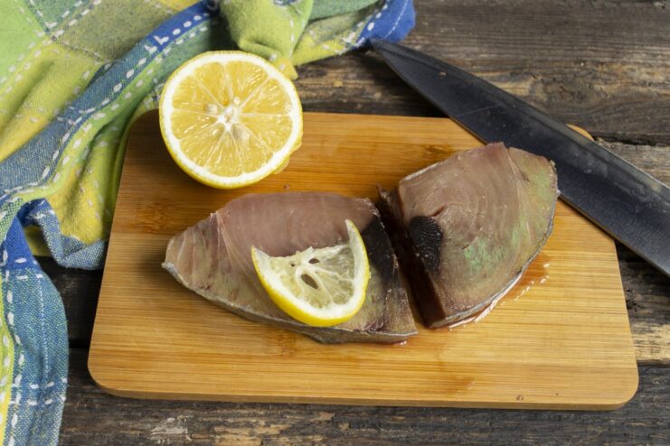 Marinating Tuna - Squeezing fresh lemon juice over the tuna steak. A hand squeezing a lemon half over a raw tuna steak to marinate it.