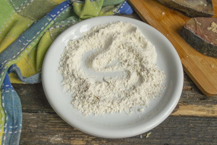 Preparing the Breading - Mixing flour with dry spices for the coating. A white plate with a mixture of all-purpose flour and dry fish seasoning.