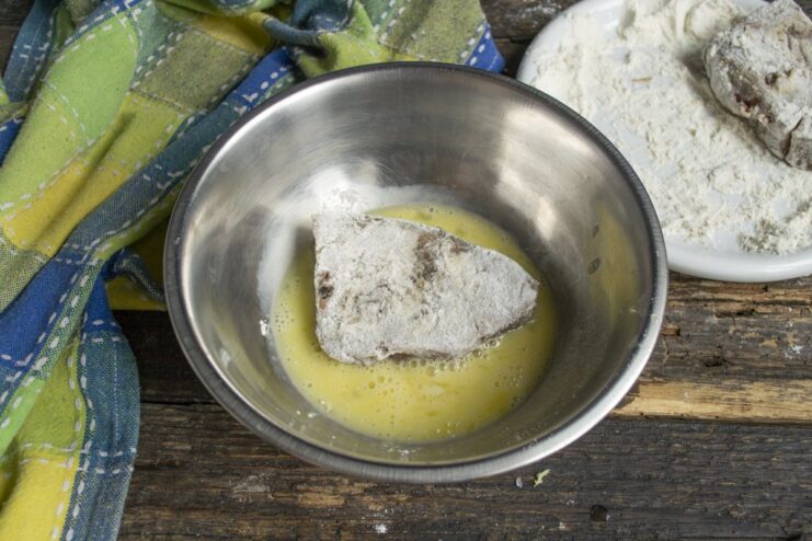 Egg Wash for Breading - Dipping the floured tuna into beaten egg. A piece of floured tuna being dipped into a bowl of beaten egg.