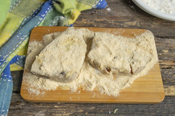 Final Breading Step - Coating the tuna steak in breadcrumbs. An egg-washed tuna steak being thoroughly coated in breadcrumbs on a wooden board.