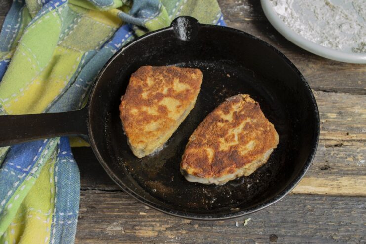 Frying the Tuna Steak - Pan-frying until golden and draining on a paper towel. Golden-brown breaded tuna steaks resting on a paper towel to absorb excess oil.