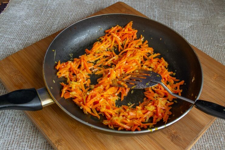 Sliced carrots, onions, and garlic being sautéed in a hot pan.