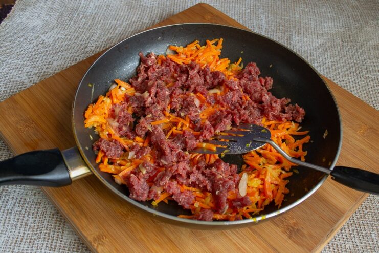 Ground beef being broken up and cooked with sautéed vegetables in a pan.