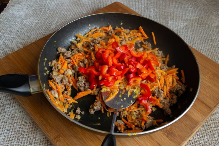 Diced bell peppers added to the pan with cooked ground beef and vegetables.