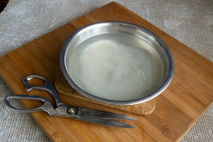 A bundle of dry glass noodles soaking in a bowl of hot water.