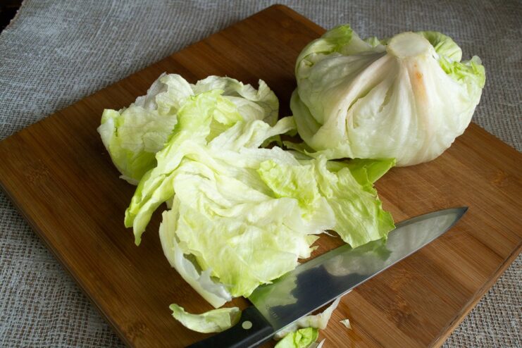 A hand slicing a roll of Iceberg lettuce leaves into thin ribbons on a cutting board.