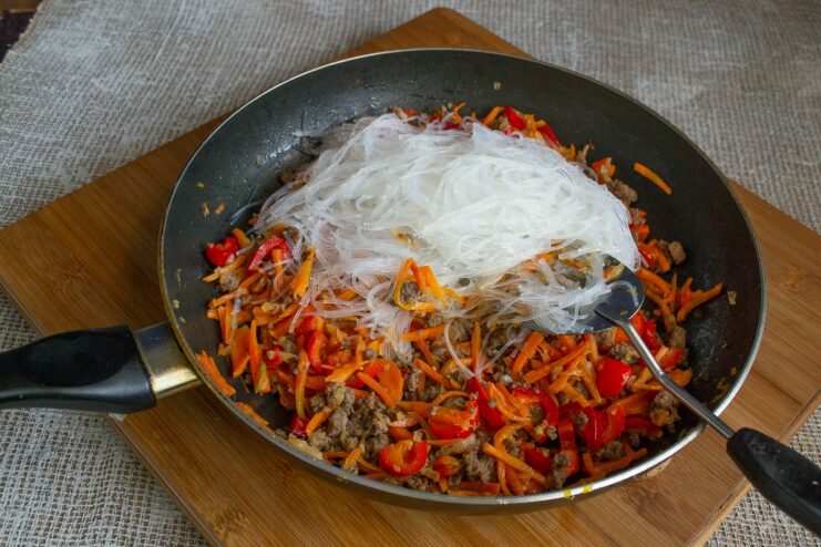 Cooked glass noodles being added to the pan with the beef and vegetable mixture.