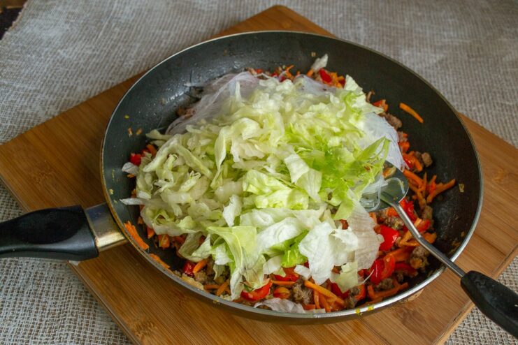 Shredded Iceberg lettuce being added to the stir-fry in the pan.
