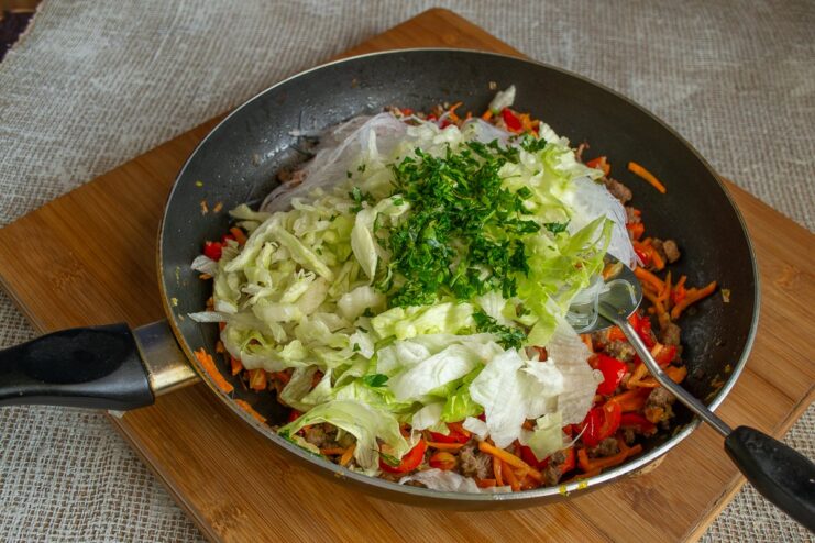 Chopped fresh dill being sprinkled over the beef and noodle stir-fry in the pan.