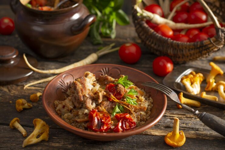 A comforting one-pot meal of pork belly and buckwheat A serving of rustic pork belly with buckwheat and mushrooms in a white bowl, garnished with fresh herbs.