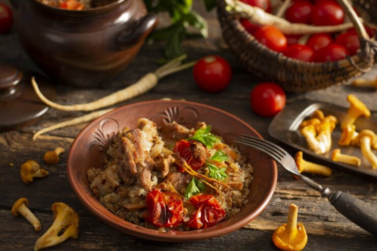 A serving of rustic pork belly with buckwheat and mushrooms in a white bowl, garnished with fresh herbs.