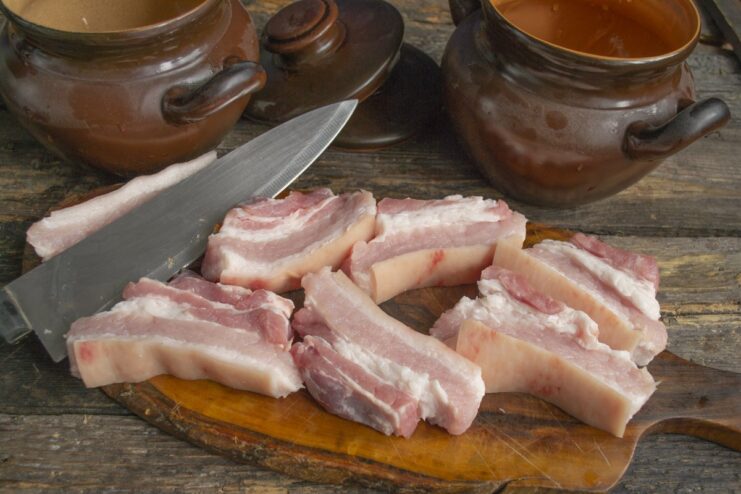 Preparing the pork belly for the rustic pot recipe Raw pork belly being sliced into thick pieces on a wooden cutting board.