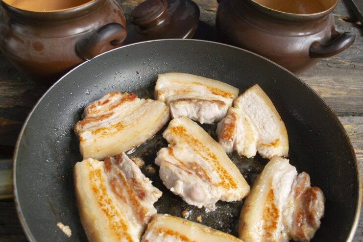 Searing pork belly to lock in flavor Slices of pork belly sizzling in a hot pan, getting a golden-brown crust.