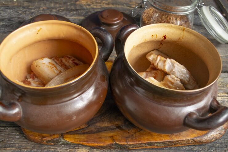 Layering ingredients in the clay pot Layering onions, carrots, and seared pork belly in a brown clay pot.