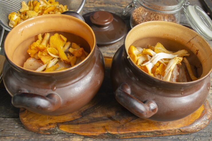 Adding chanterelles for an earthy flavor Fresh chanterelle mushrooms being added on top of the pork belly in a clay pot.