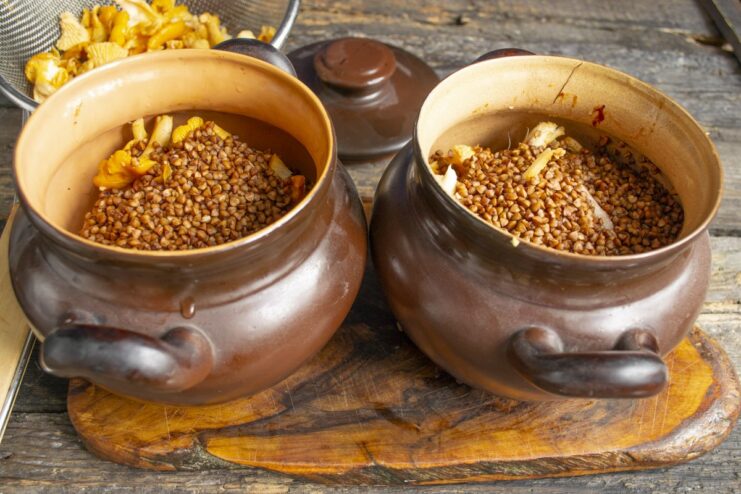 Adding buckwheat groats to the pot Dry buckwheat groats being poured over the layers of meat and mushrooms in a clay pot.