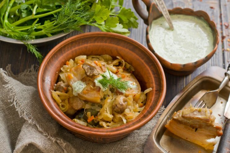 A plate of ready-to-eat pork belly with stewed cabbage and mushrooms, garnished with fresh dill.