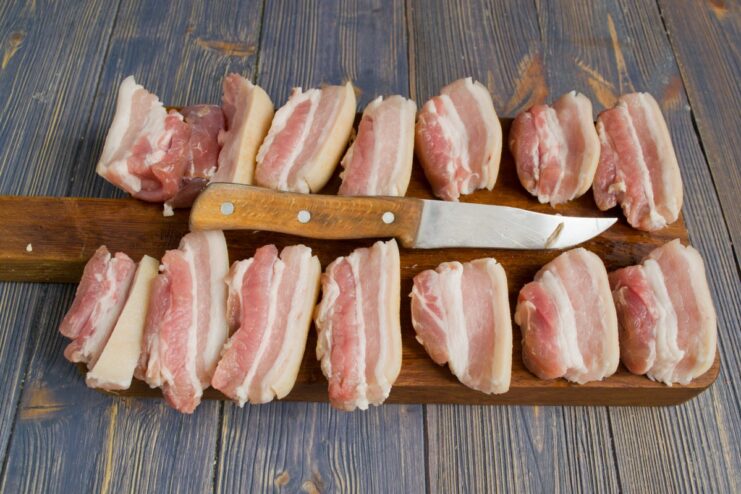 Preparing the Pork Belly: Slicing and Patting Dry Raw pork belly sliced into pieces on a cutting board, being patted dry with paper towels.
