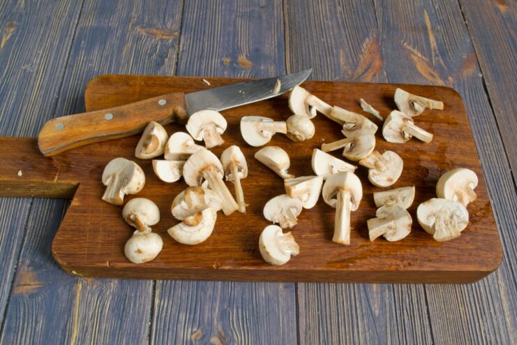 How to Prepare Mushrooms for Stewing Fresh champignon mushrooms being cut into quarters on a wooden cutting board.