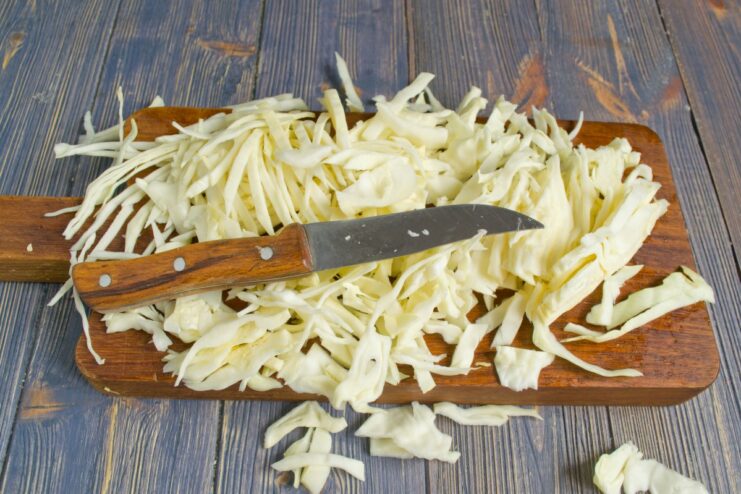 Shredding Cabbage for the Stew A head of white cabbage being thinly shredded with a knife on a cutting board.