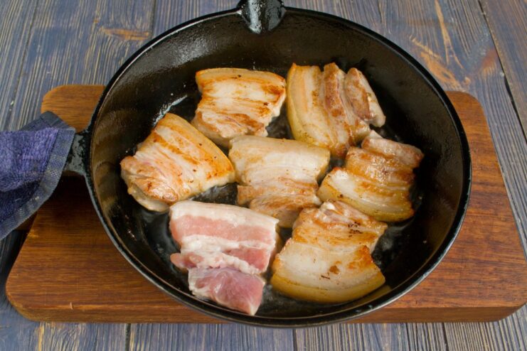Searing Pork Belly Until Golden Brown Pieces of pork belly searing in a hot skillet until golden brown and crispy.