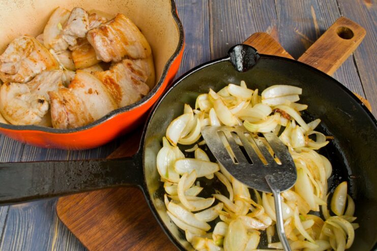 Sautéing Onions Until Caramelized Chopped onions being sautéed in a skillet with rendered pork fat until golden.