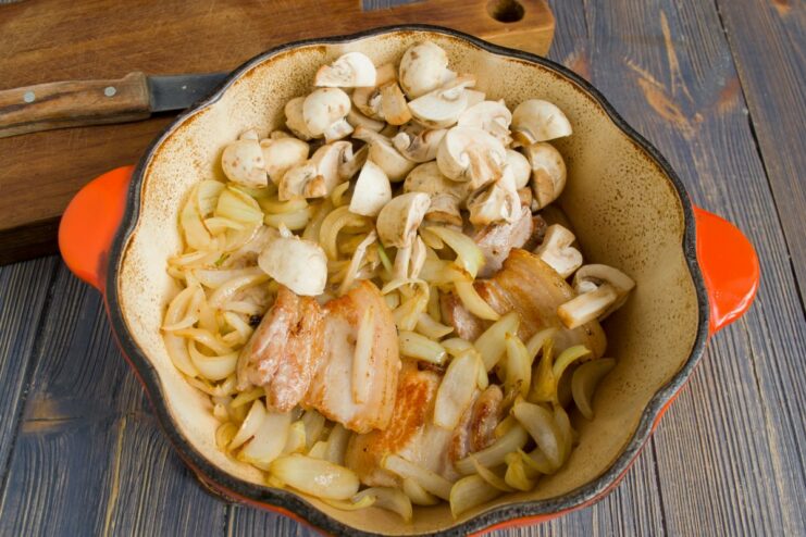 Adding Mushrooms to the Dutch Oven Sliced mushrooms being added to a Dutch oven with other ingredients for the stew.