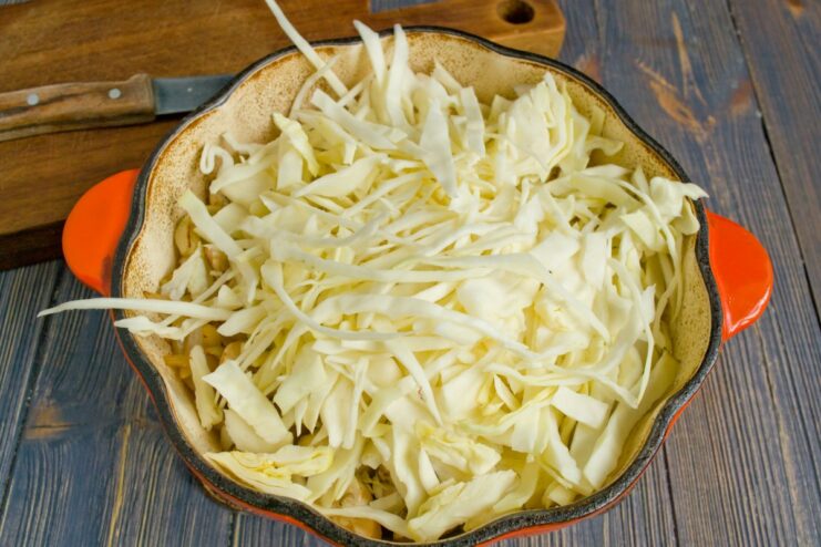 Adding Shredded Cabbage to the Pot Shredded white cabbage being added to the Dutch oven with pork and mushrooms.