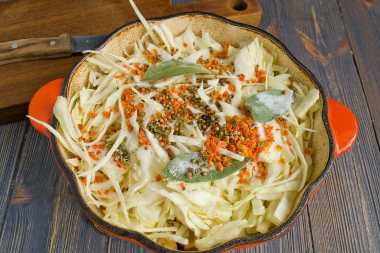 Seasoning the Pork and Cabbage Stew Spices like bay leaves and caraway seeds being added to the pot with pork and vegetables.