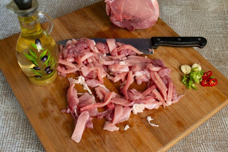 Marinating Sliced Pork with Olive Oil, Pepper, Chili, and Garlic Sliced raw pork in a bowl being seasoned with spices, chili, and garlic.