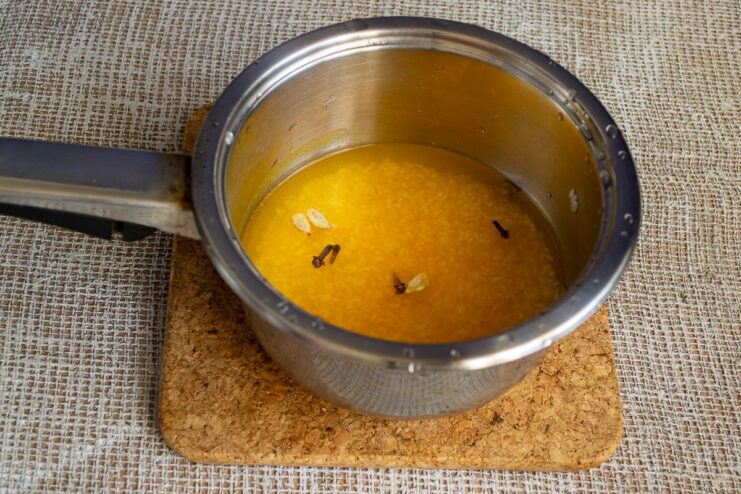Cooking Arborio Rice with Turmeric, Cloves, and Cardamom for the Stew A saucepan with yellow rice and whole spices cooking on a stove.