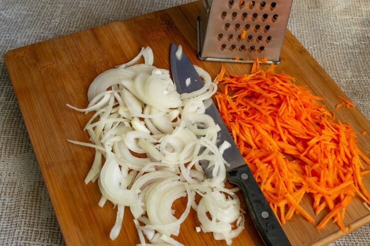 Preparing Vegetables: Slicing Onions and Grating Carrots for the Stew A cutting board with thinly sliced onions and grated carrots.