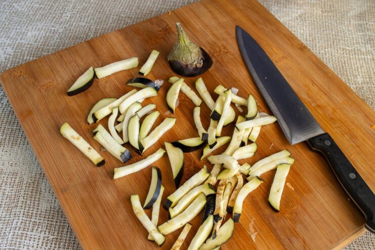 How to Cut Eggplant into Large Strips for a Hearty Stew A hand cutting an eggplant into thick strips on a wooden board.