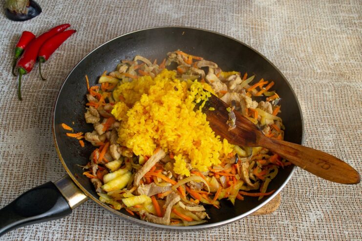 Combining Cooked Rice with the Pork and Vegetable Stew Adding cooked yellow rice to the pan with the pork and vegetable mixture.