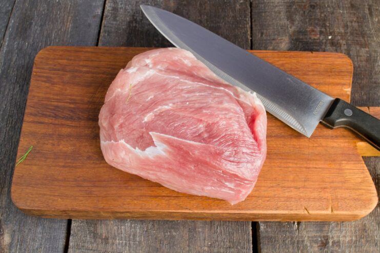 Properly drying the pork tenderloin ensures a perfect sear. A piece of raw pork tenderloin being patted dry with a paper towel on a cutting board.