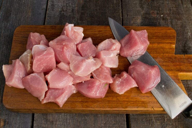 Cutting pork into large cubes for the Chinese-style recipe. Diced raw pork tenderloin on a wooden cutting board.