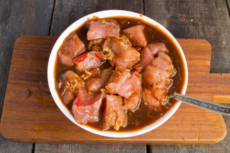 Let the pork marinate in the fridge to absorb all the flavors. A bowl of diced pork marinating in a dark sauce.
