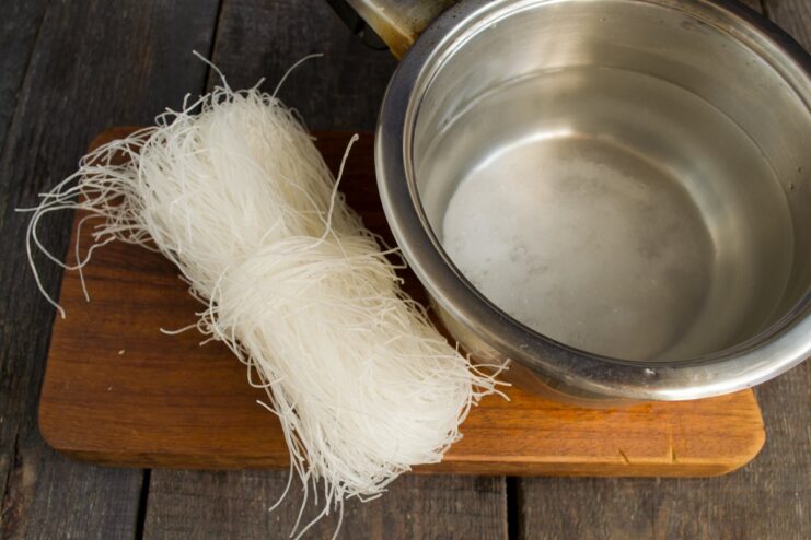 Cooking the funchoza (glass noodles) until tender. Funchoza glass noodles being boiled in a pot of water.