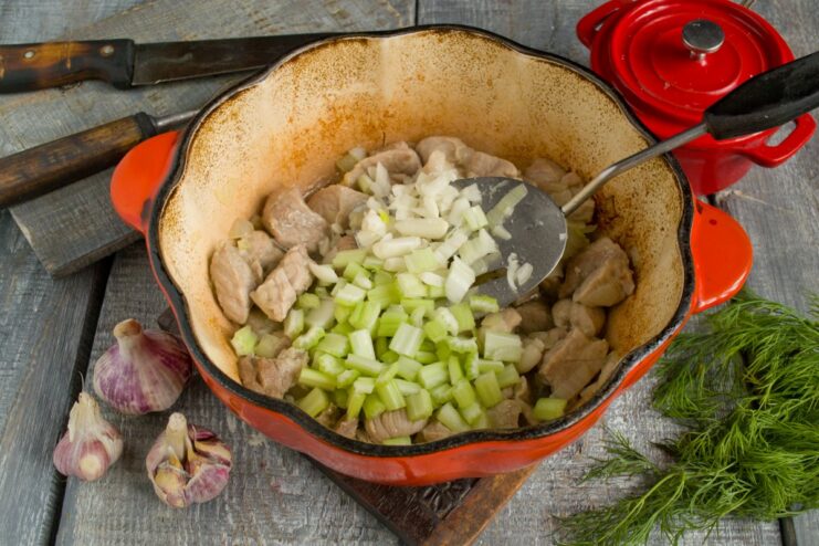 Adding Garlic and Celery for an Aromatic Stew Chopped garlic and celery being added to the pork and onions in the pan.