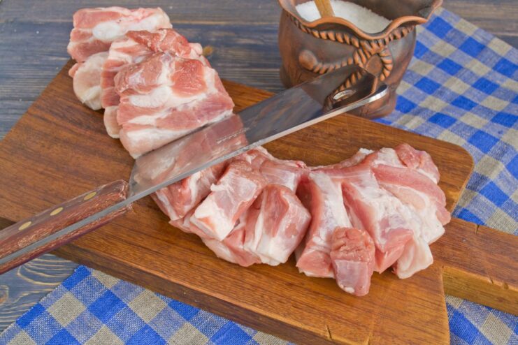 Preparing Pork: Slicing into Portions Raw pork being cut into individual pieces on a cutting board.