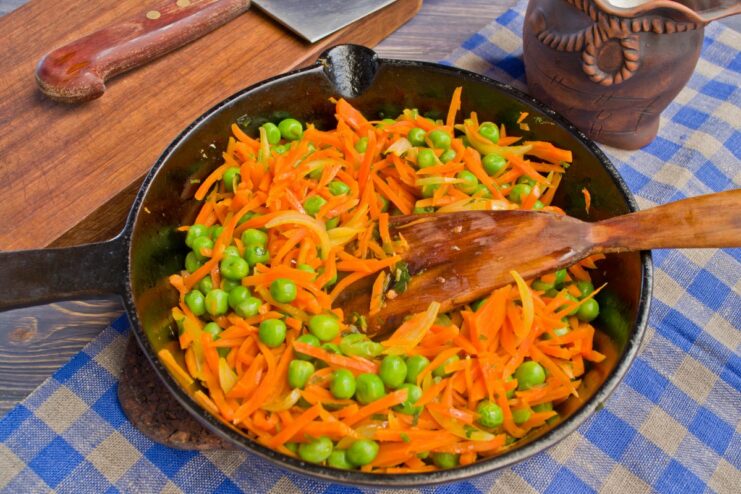 Adding Green Peas to the Sautéed Vegetables Frozen green peas being added to the pan with sautéed carrots and onions.