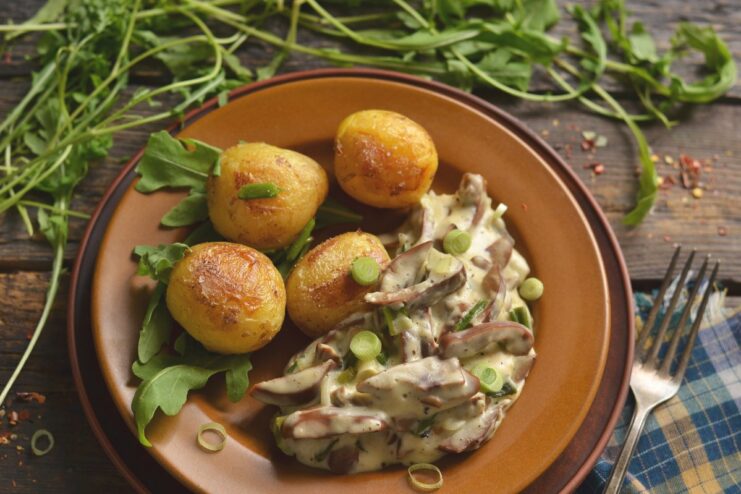 A plate of pork kidneys in a creamy sour cream sauce, served with potatoes and garnished with herbs.
