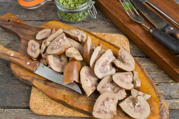 Preparing the Pork Kidneys for Cooking Close-up of cooked pork kidneys being sliced thinly on a cutting board.