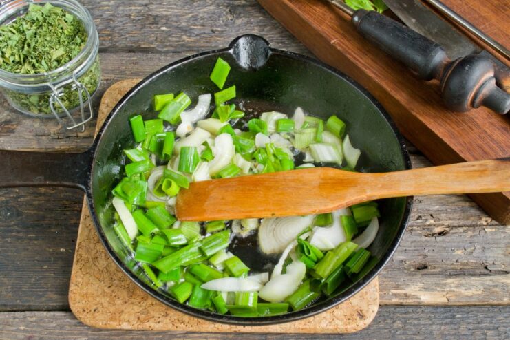 Building the Flavor Base by Sautéing Onions Chopped green onions being sautéed in a hot skillet with oil and butter.