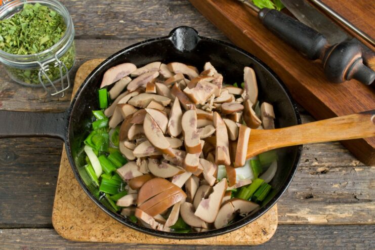 Browning the Kidneys to Lock in Flavor Sliced pork kidneys and green onions being fried together in a cast-iron skillet.