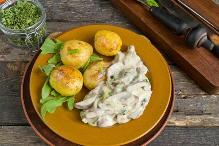 The Finished Dish: Pork Kidneys in Sour Cream with Potatoes A serving of pork kidneys in sour cream sauce next to golden-fried potatoes, garnished with fresh herbs.