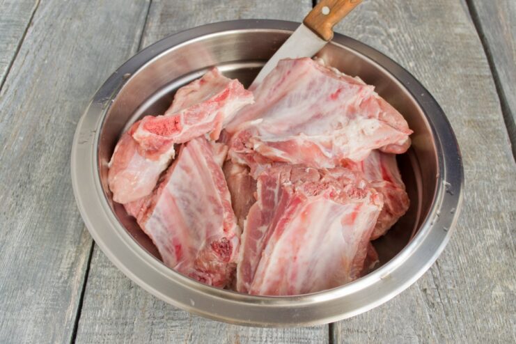 Preparing Pork Ribs by Cutting Them into Smaller Sections A rack of raw pork ribs on a cutting board being cut into smaller sections.