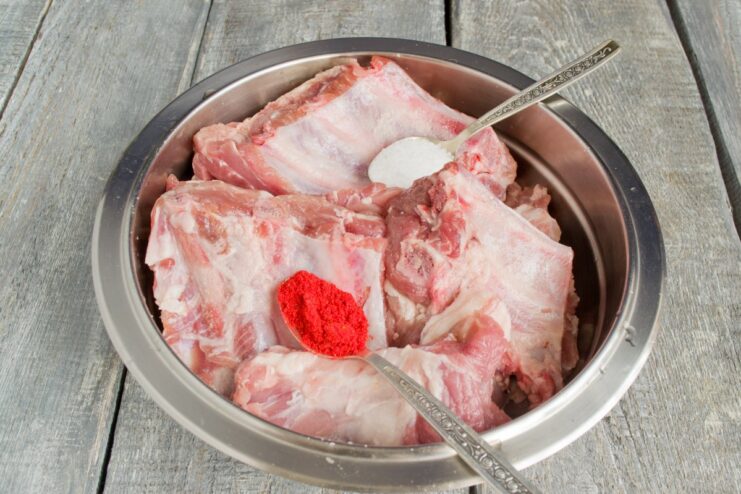 Seasoning Pork Ribs with a Dry Rub of Salt and Paprika Close-up of hands rubbing a spice mix of salt and paprika onto raw pork ribs.
