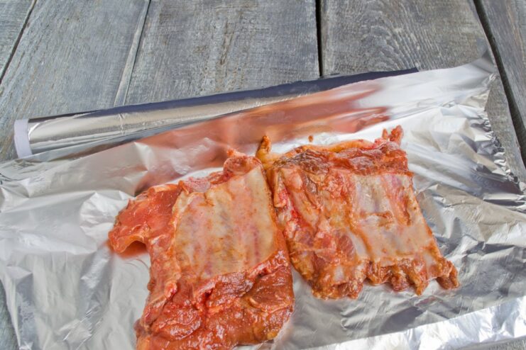 Wrapping Pork Ribs in Foil for Tender, Juicy Results A section of marinated pork ribs being wrapped tightly in aluminum foil before baking.